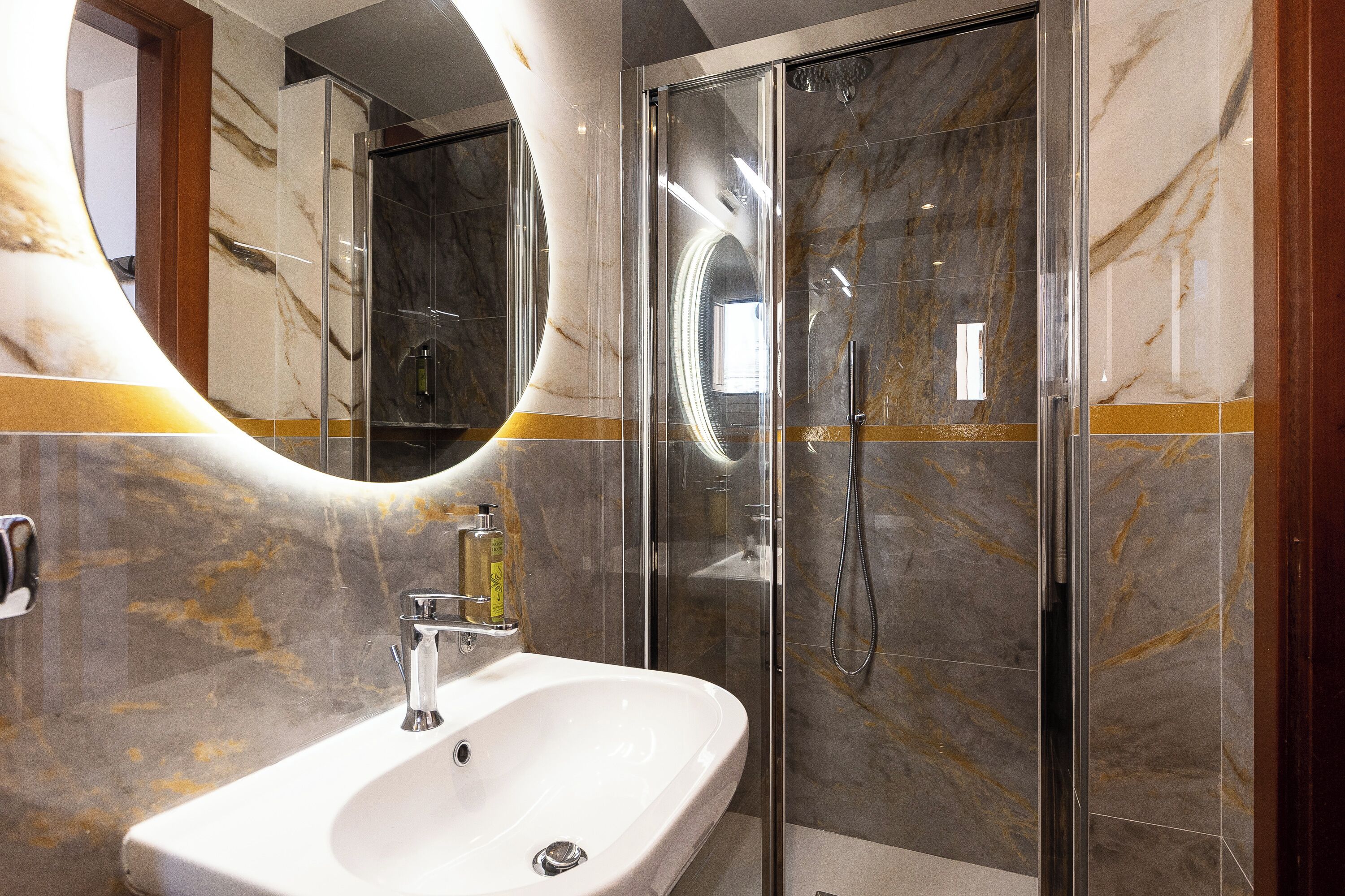 A modern bathroom with a marble vanity, a glass shower enclosure, and a large mirror.