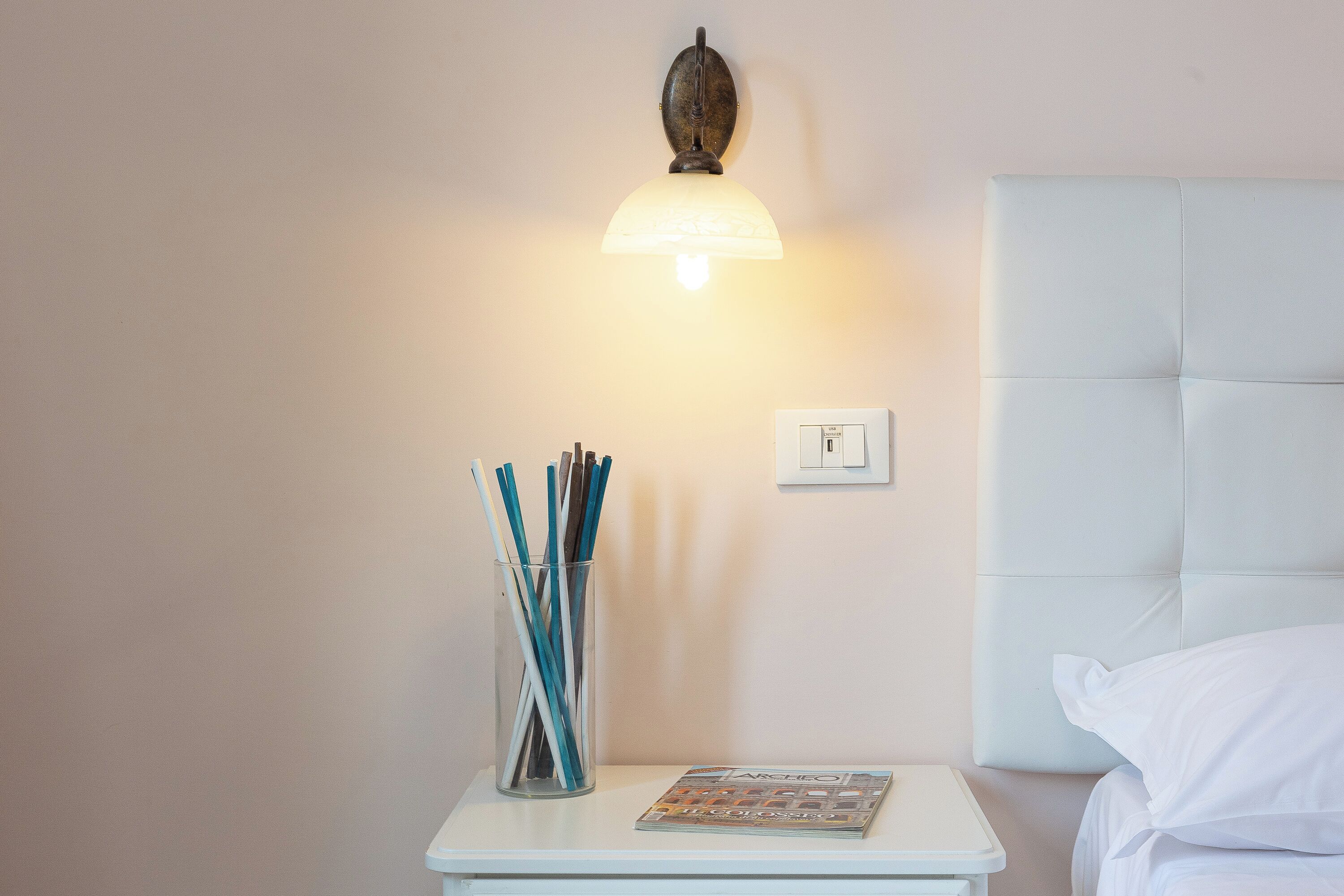 A neatly arranged bedside table with a lamp, a glass container with pens, and a magazine.