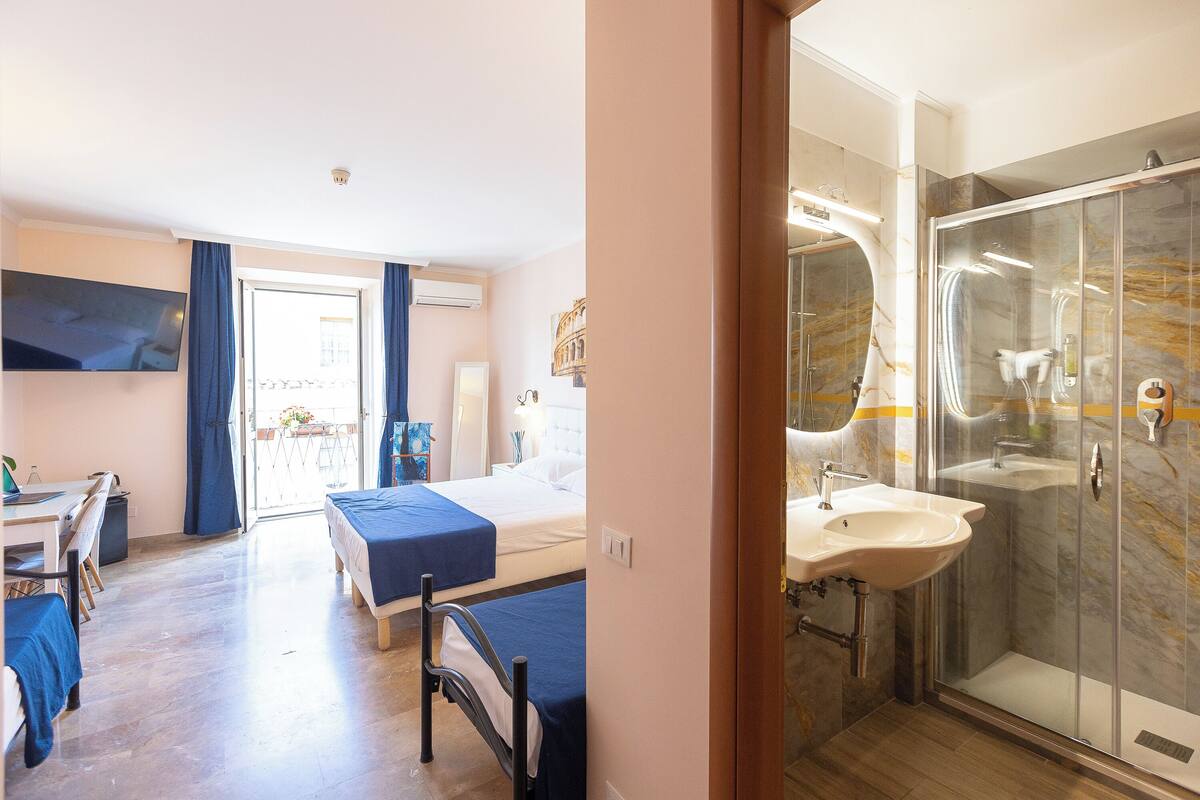 Une chambre d’hôtel comprenant un lit, un bureau, une chaise, une douche avec une porte en verre et un lavabo.