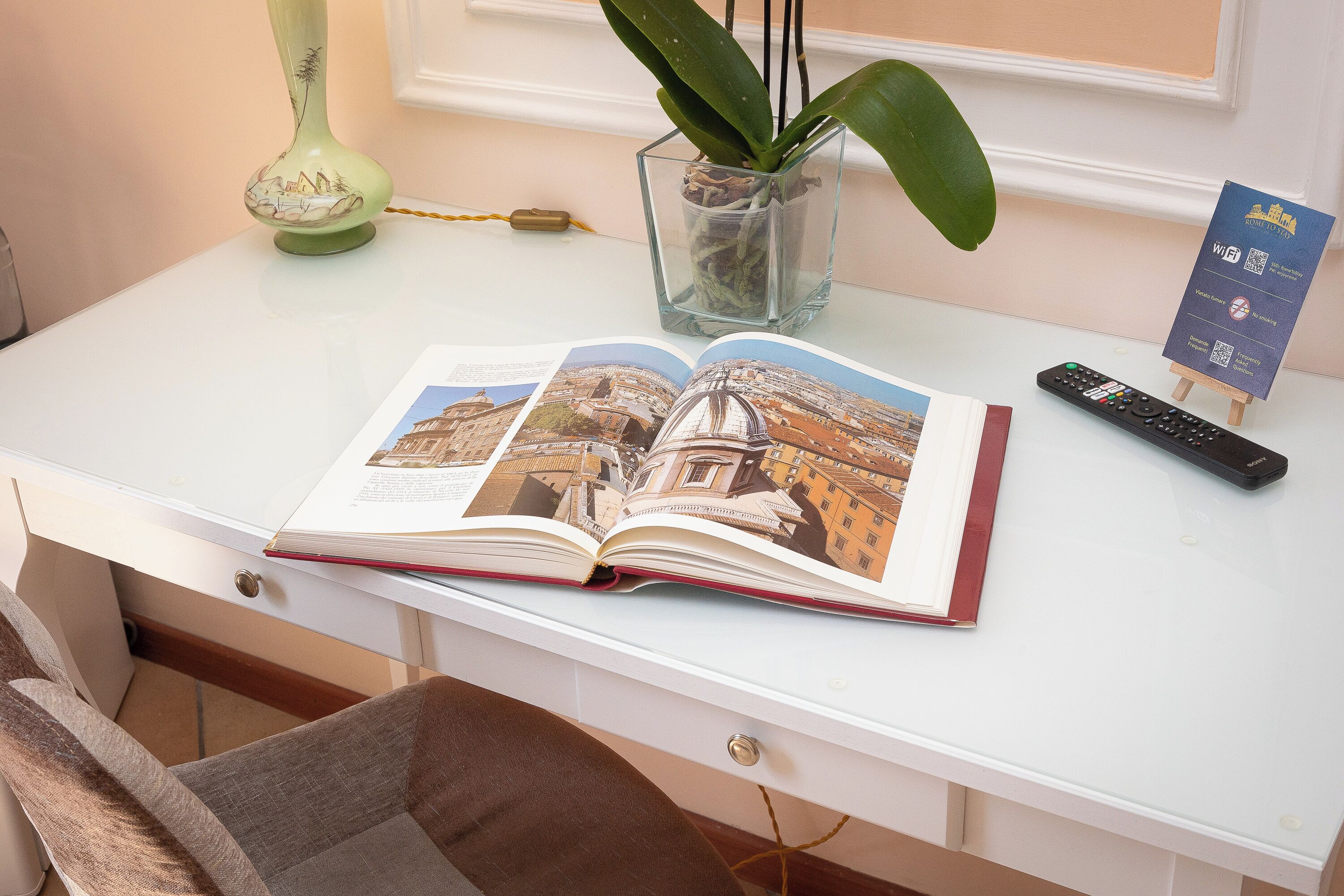 A desk with a book, a remote control, a vase with a plant, and a sign with Wi-Fi information.