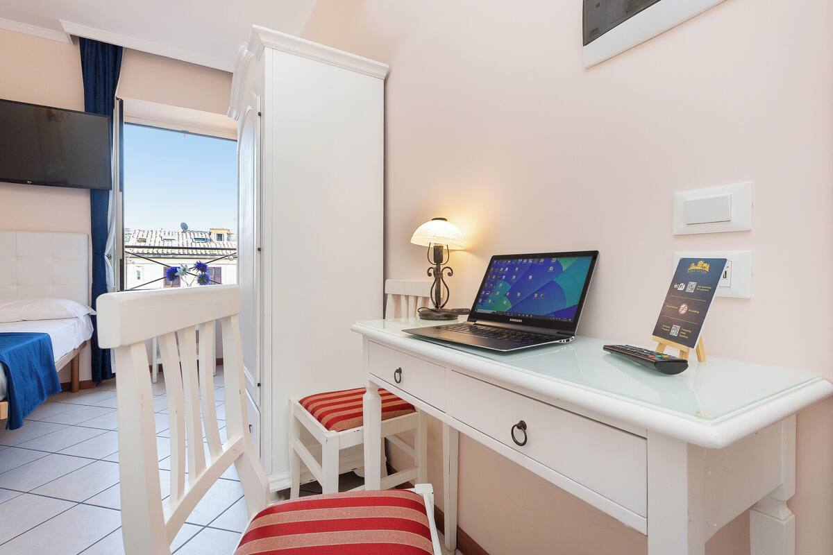 Une chambre d’hôtel avec un lit, un bureau avec un ordinateur portable, une chaise, une lampe et une vue sur la ville.