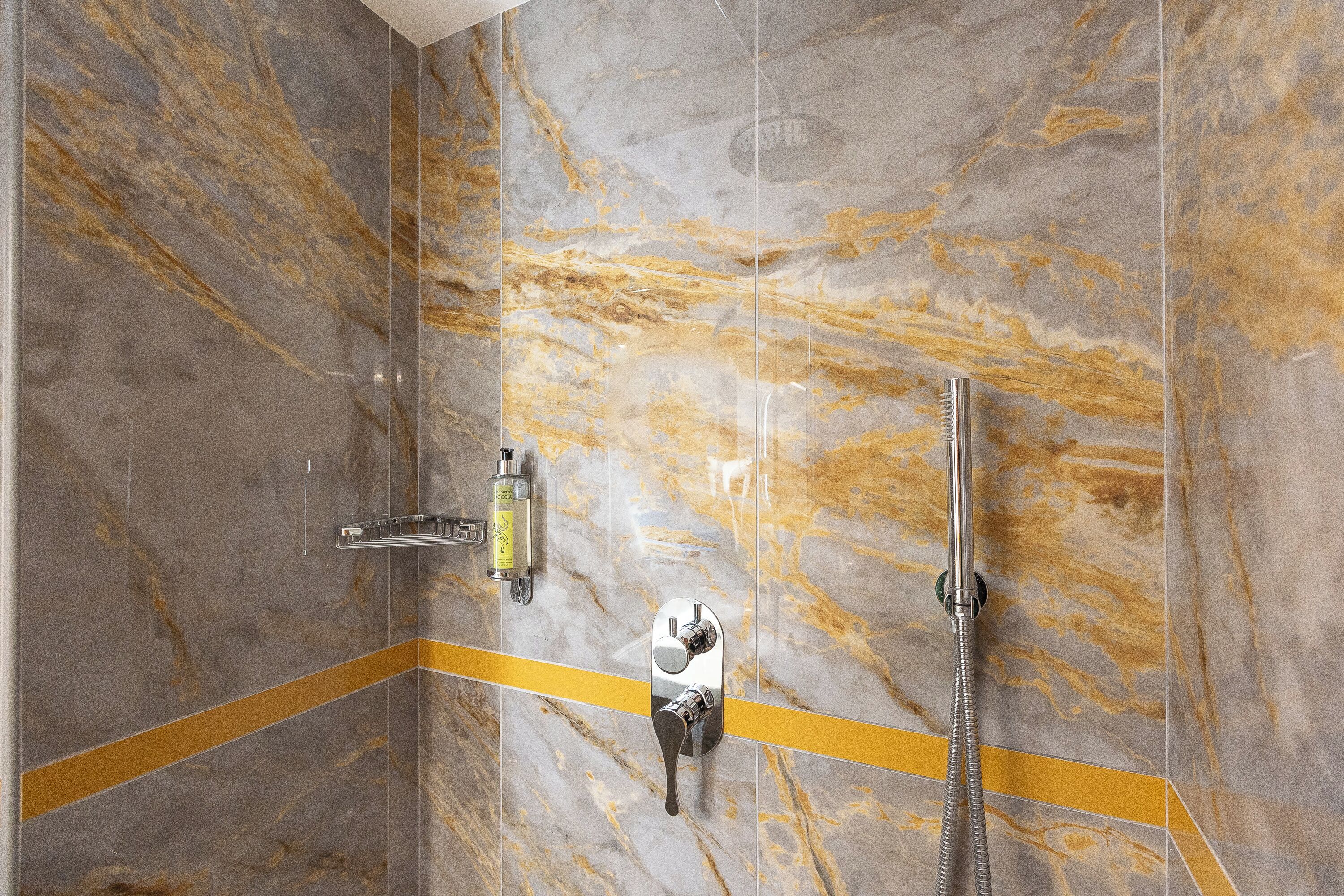 A shower with a marble wall, a yellow accent strip, and a handheld showerhead.