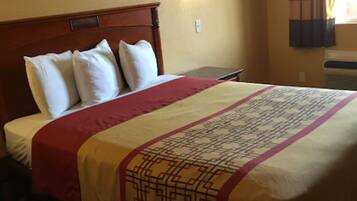 A hotel room with a wooden headboard, a bed with a patterned bedspread, a wall-mounted light, and a framed picture above the bed.