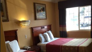 A hotel room with two beds, a nightstand, a lamp, a painting on the wall, and a window with curtains. - National City Motel (National City)