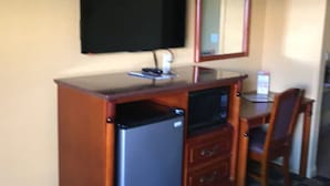 A compact room with a wooden desk, a refrigerator, a microwave, a television, and a mirror. - National City Motel (National City)