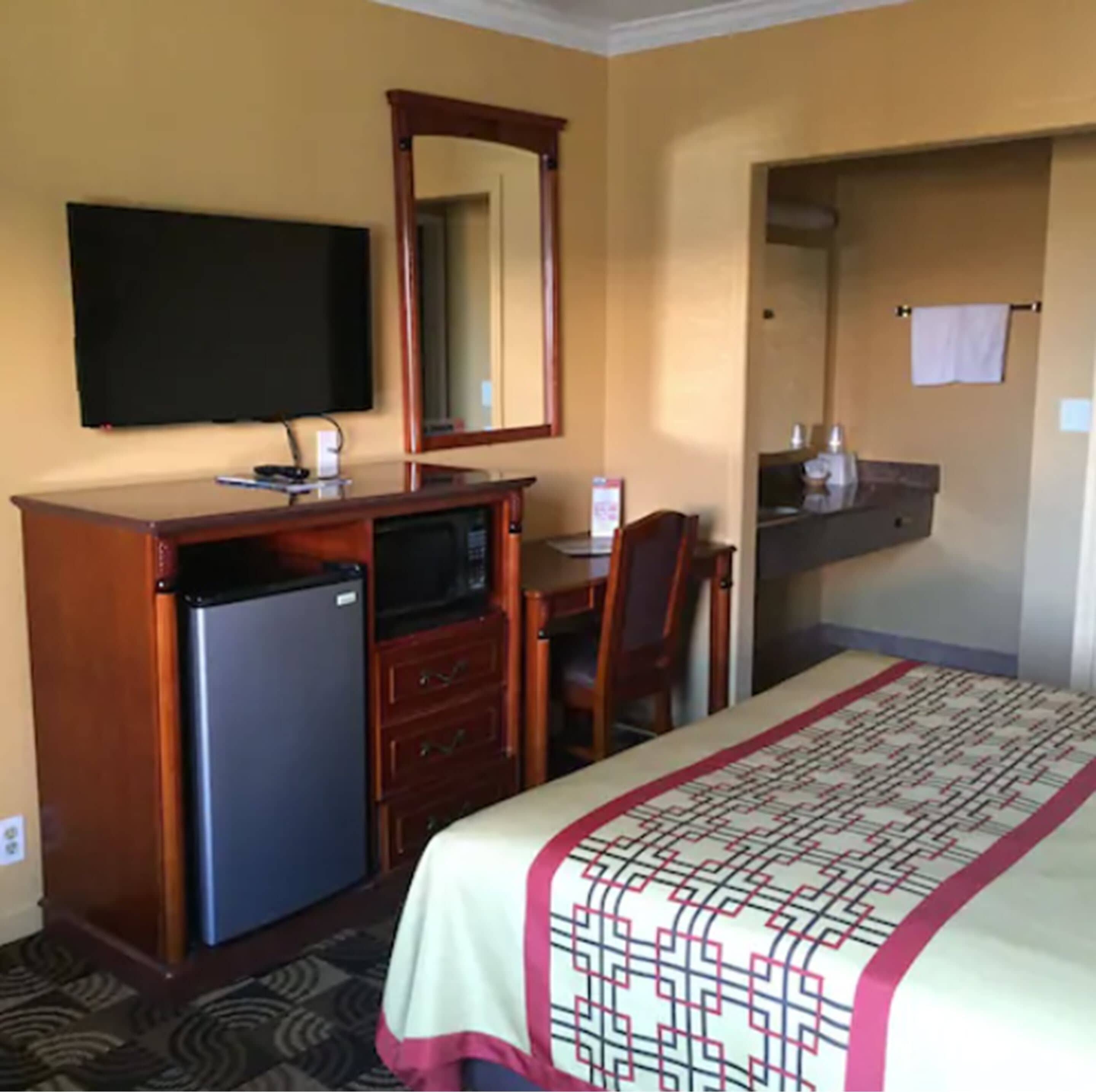Une chambre d’hôtel équipée d’un lit, d’un bureau avec un ordinateur, d’un réfrigérateur, d’une télévision et d’un miroir.