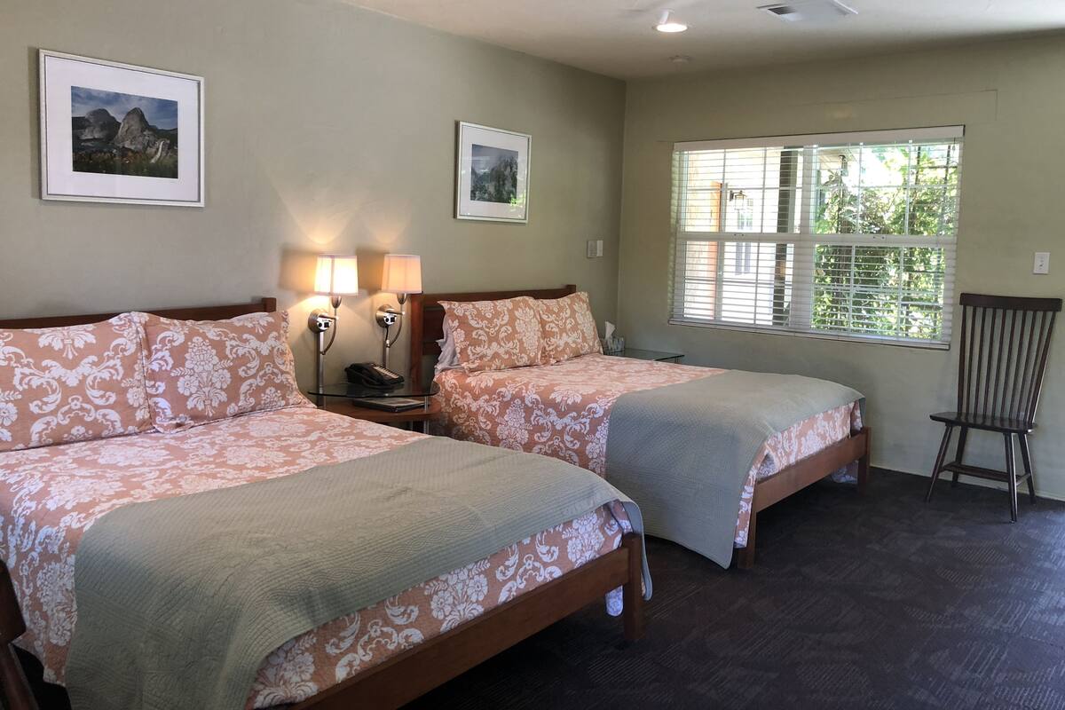 A hotel room with two beds, a ceiling fan, and two wall-mounted lamps.