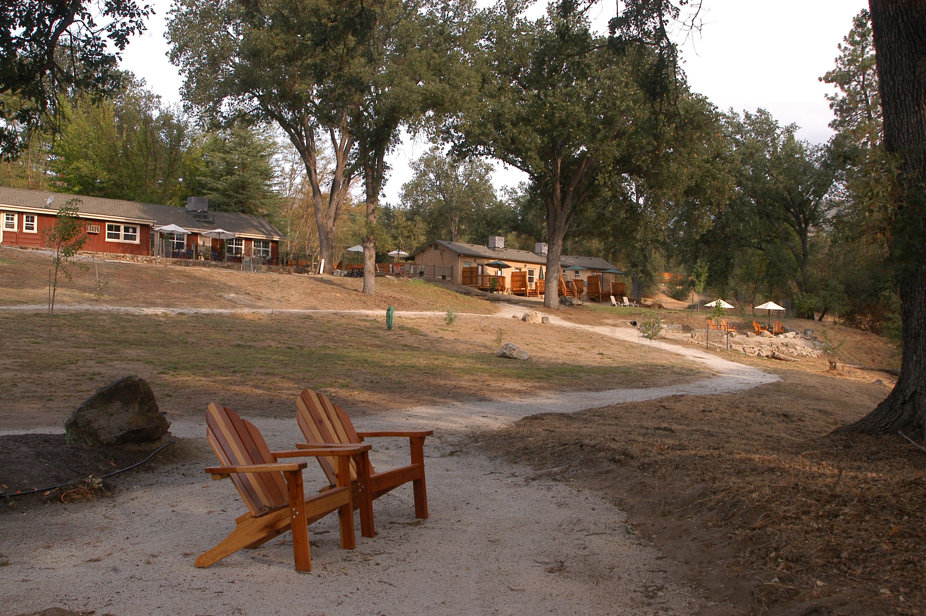 A rustic lodge with a dirt path leading to a wooden deck with two Adirondack chairs.