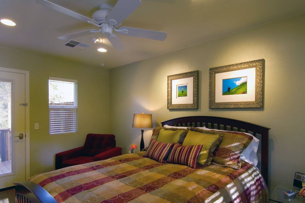A bedroom with a bed, a chair, a ceiling fan, and two framed pictures on the wall.