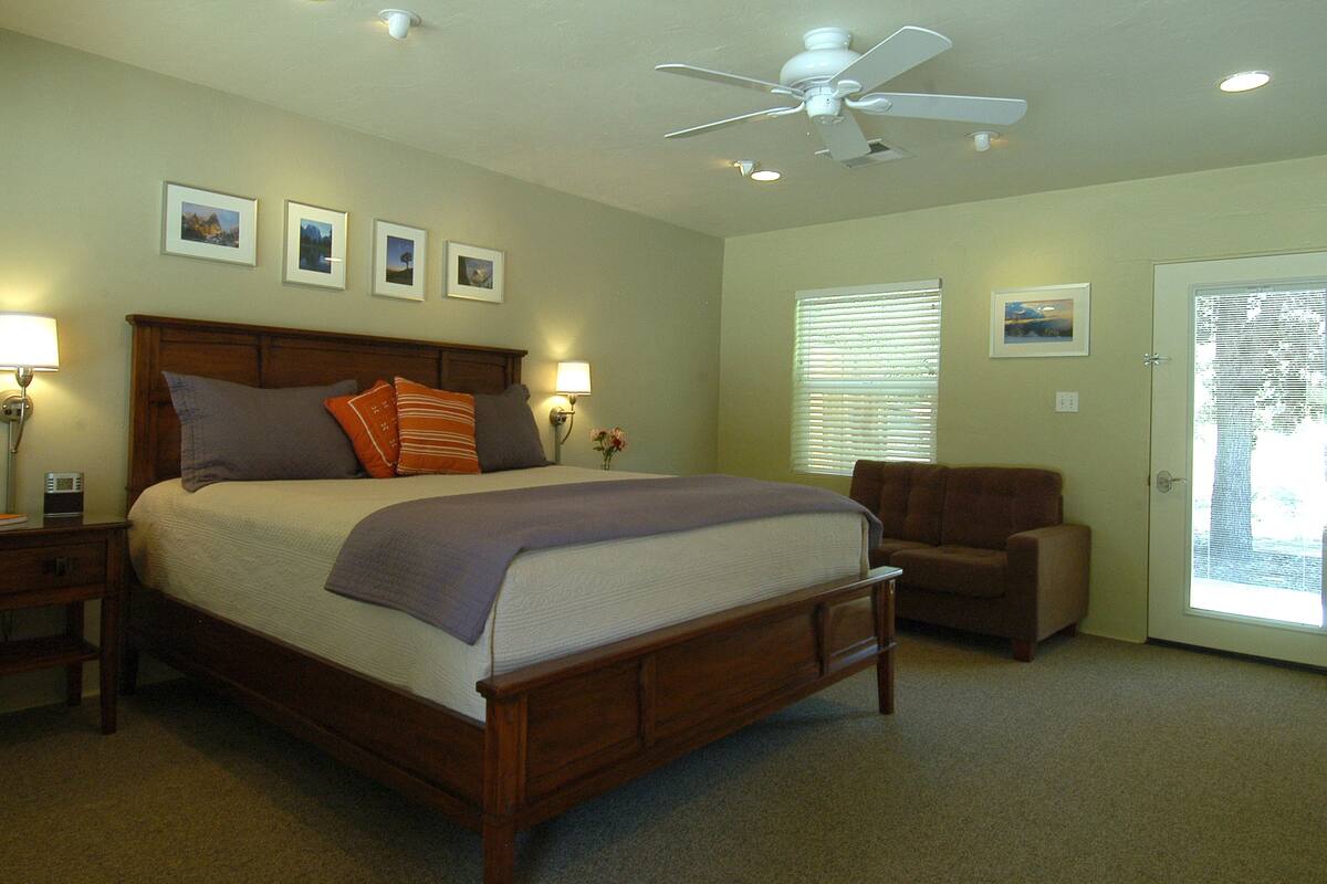 A bedroom with a bed, nightstands, a chair, a ceiling fan, and wall-mounted lamps.