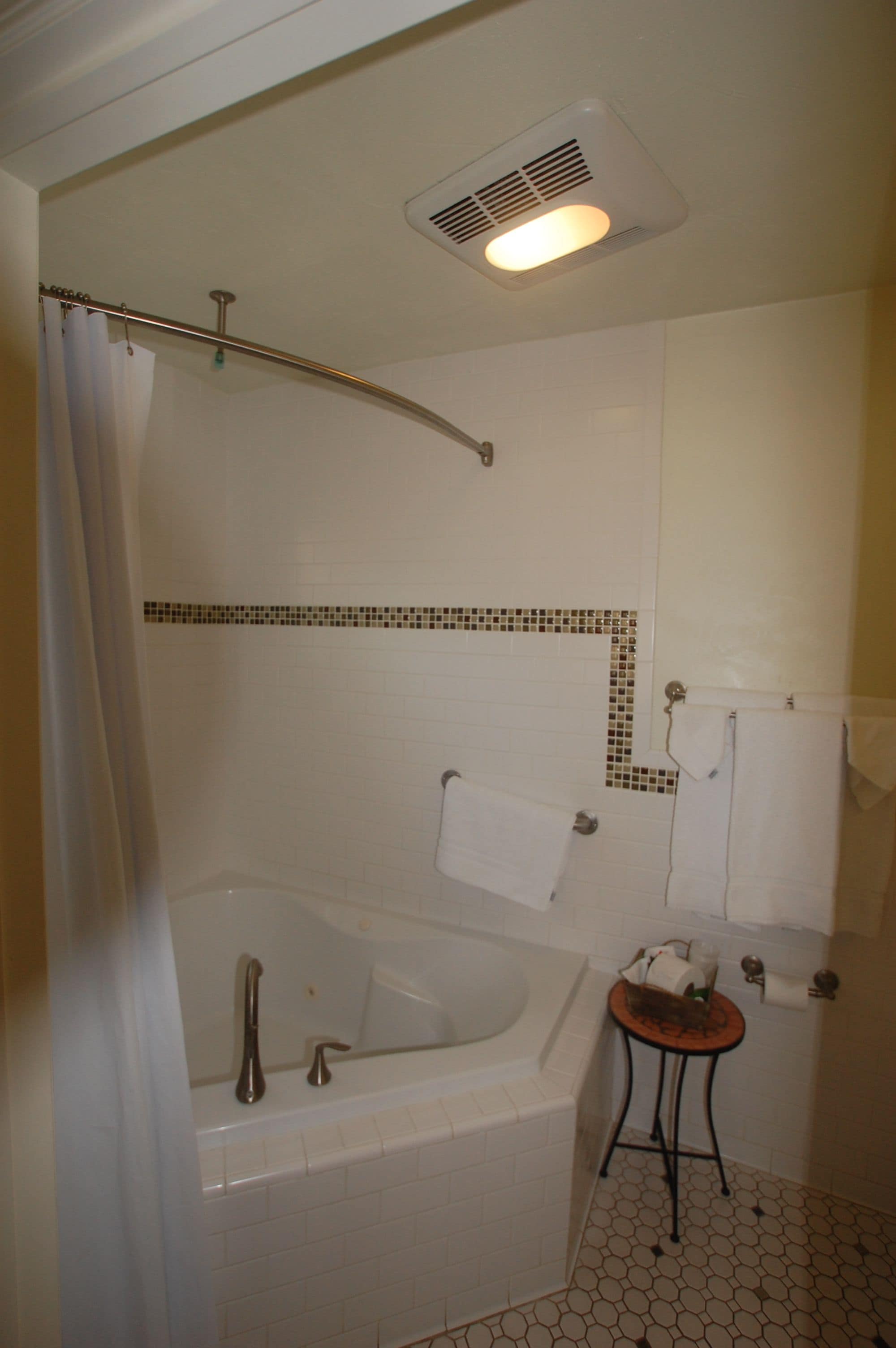 Un baño con bañera, cortina de ducha, toallero y una mesita con artículos de aseo.