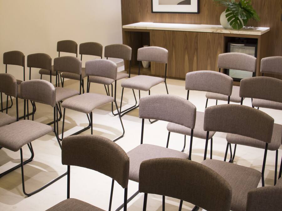 A conference room with rows of chairs, a projector, a wooden panel wall, and a framed picture.