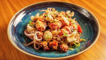 Un plato de comida con diversos ingredientes, entre ellos lo que parece ser pulpo, verduras y posiblemente algún tipo de carne, servido en un plato de cerámica azul.