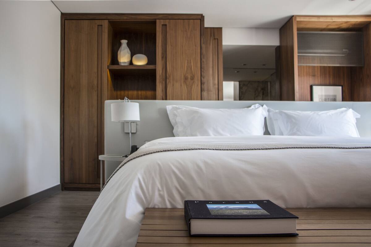 A modern hotel room with a large bed, wooden wardrobe, and a bedside table with a lamp.