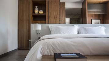 Una habitación de hotel moderna con una cama grande, un armario de madera y una mesita de noche con lámpara.
