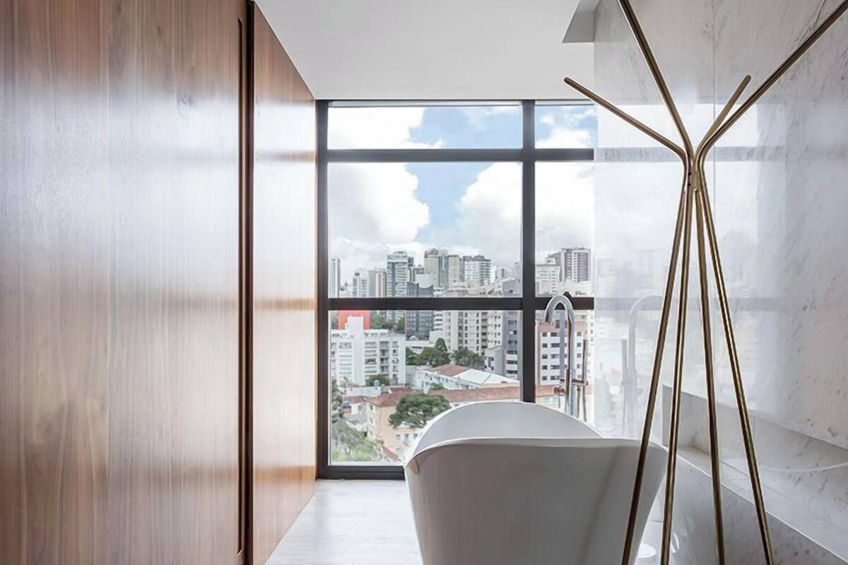 A modern interior with a large window, a white bathtub, and a geometric floor lamp.
