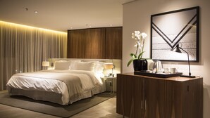 Una habitación de hotel moderna con una cama grande, una mesita de noche de madera, un escritorio con una lámpara y una obra de arte enmarcada en la pared.