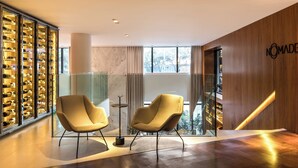 A modern interior with two armchairs, a wine display, and a wooden wall with the text "NOMADE". - Nomaa Hotel (Curitiba)
