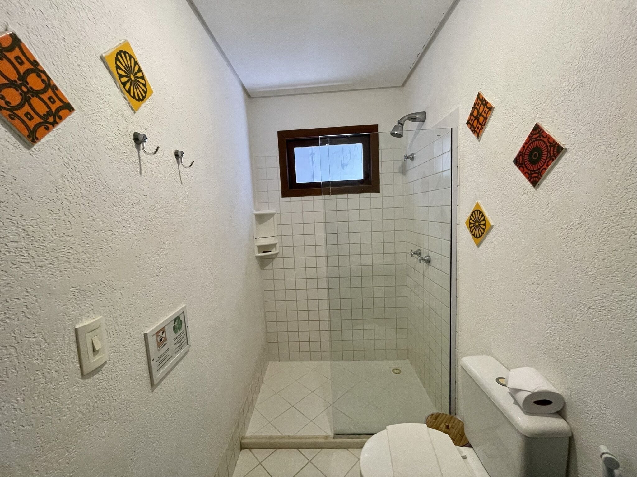 Un baño pequeño con azulejos, ducha, inodoro y ventana.