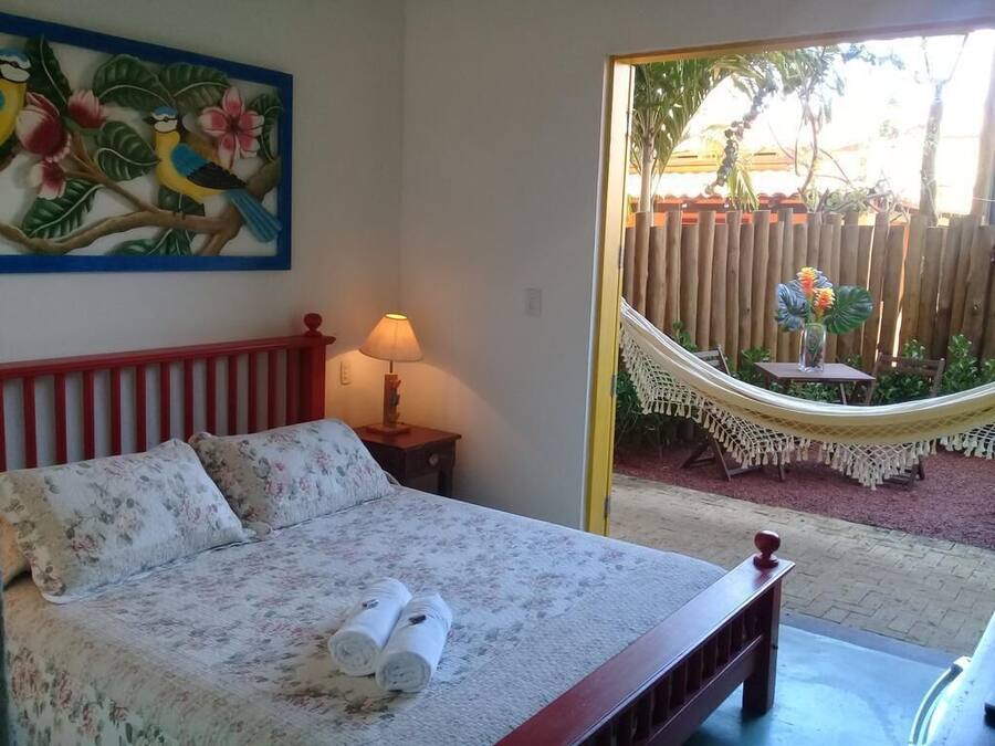 A bed with floral bedding, a hammock, and a view of a garden with a wooden fence.