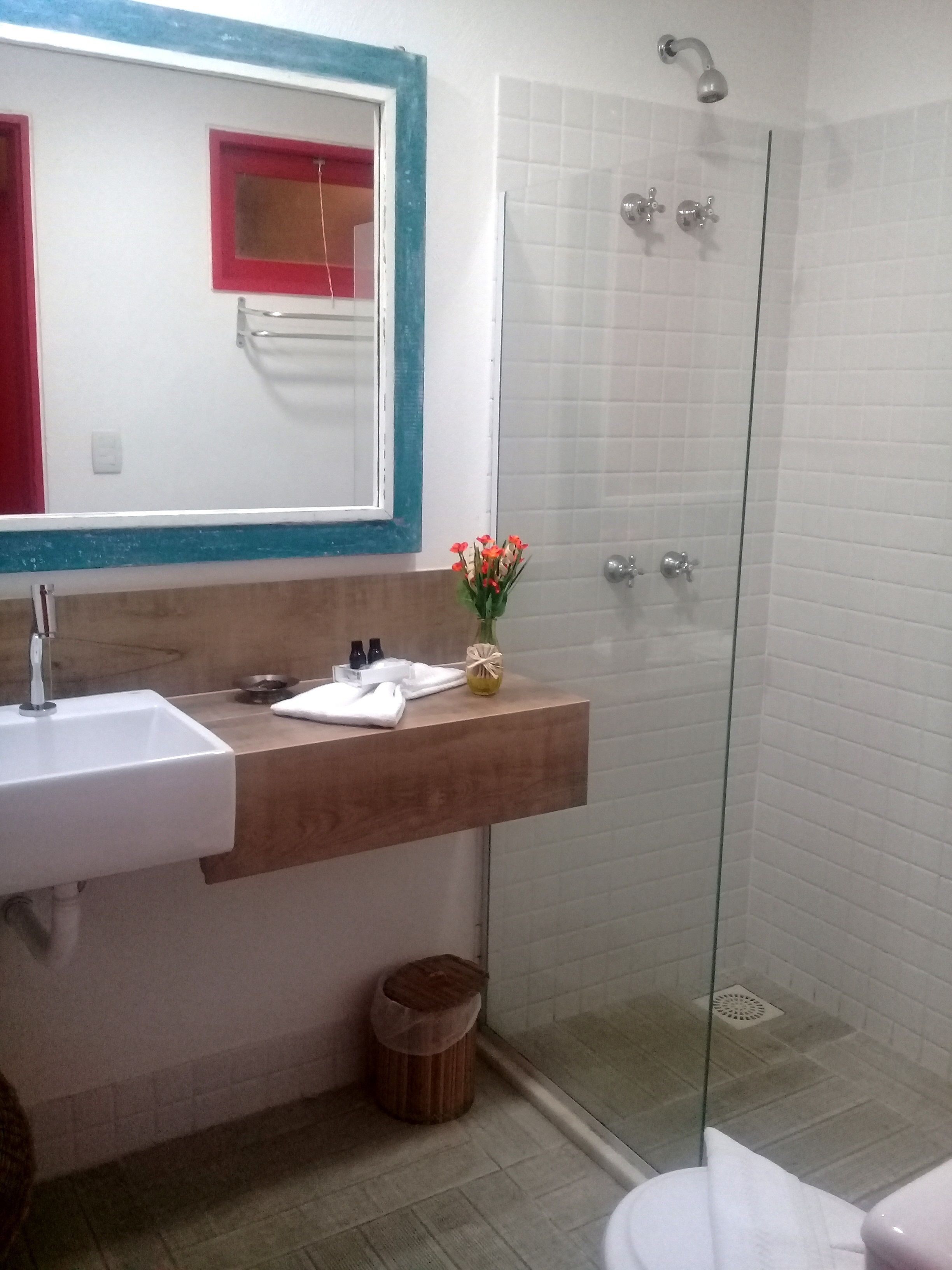 Un baño con lavamanos blanco, tocador de madera, cabina de ducha de vidrio y espejo con marco rojo.