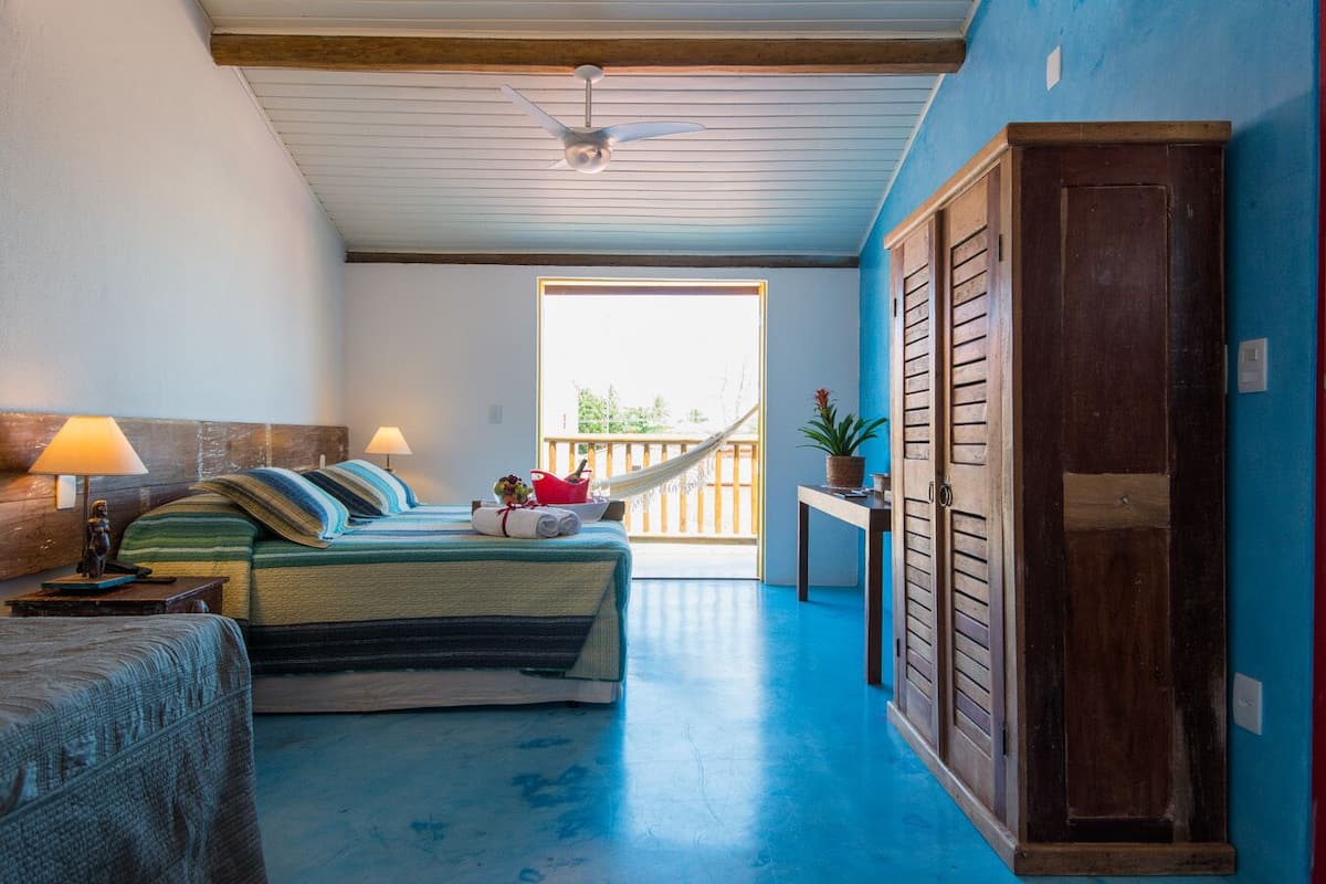 A bedroom with a bed, a nightstand, a lamp, a window, and a view of the outdoors.