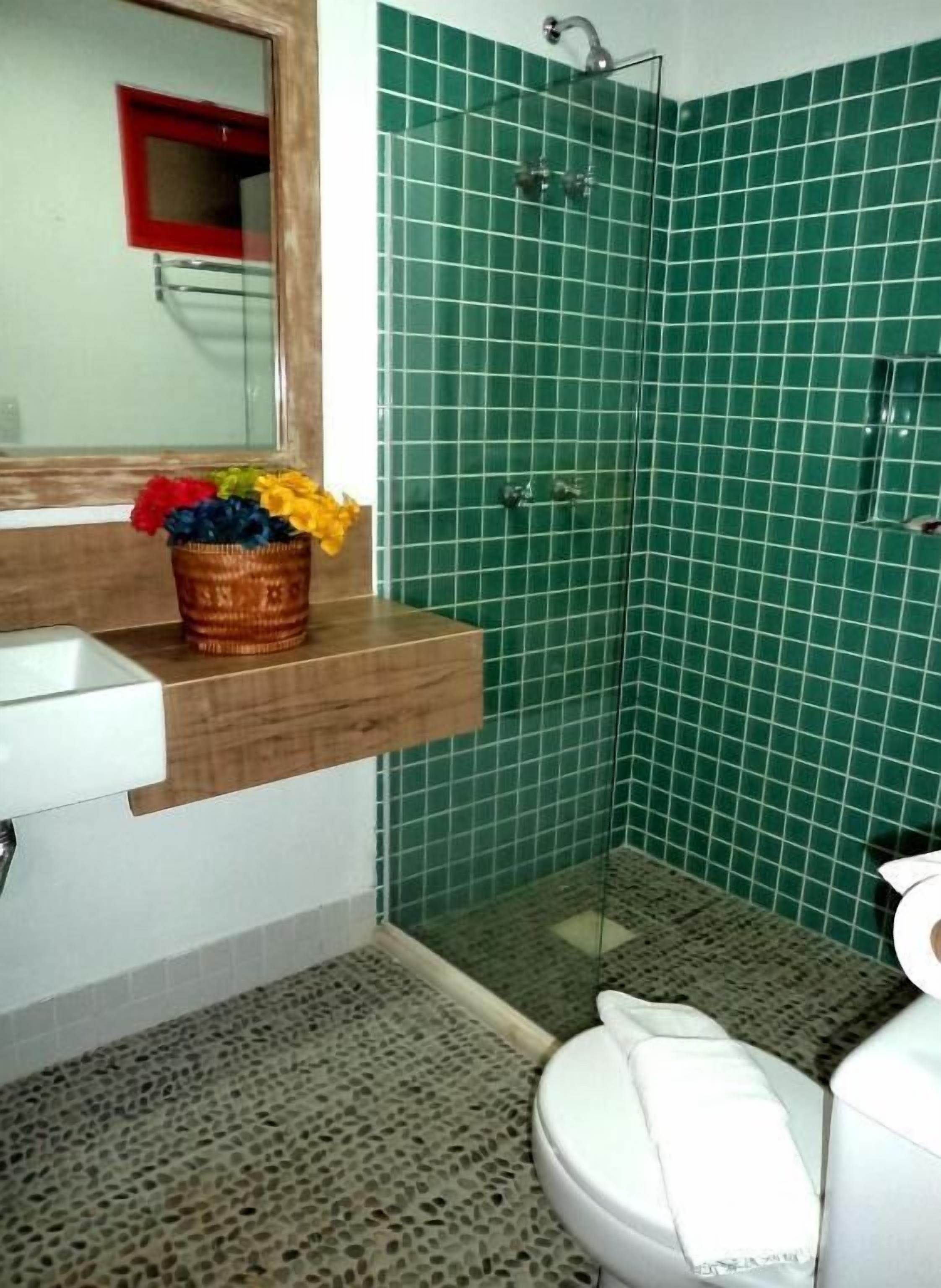A bathroom with a green tiled shower, a wooden vanity with a sink, and a toilet.