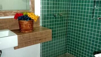 A bathroom with a green tiled shower, a wooden vanity with a sink, and a toilet.