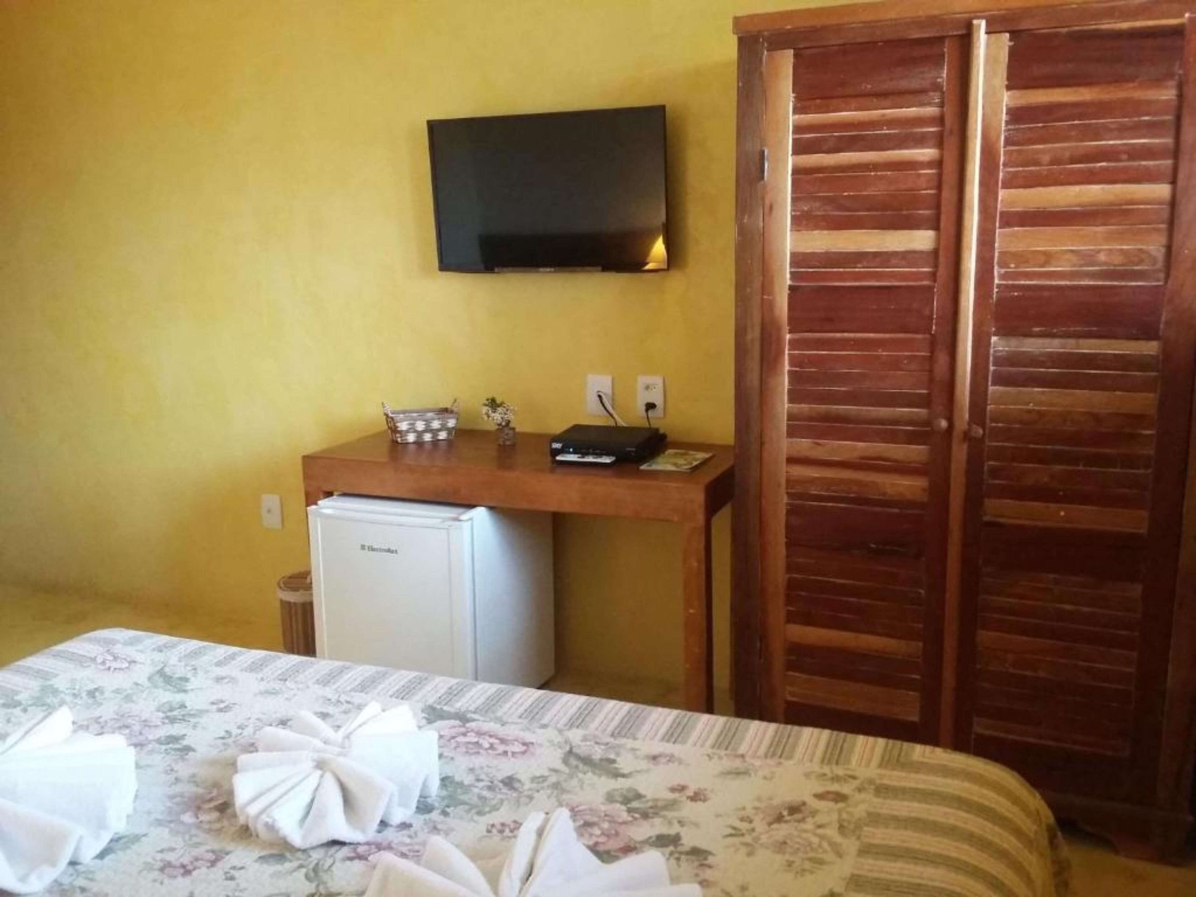 Una camera d'albergo con un letto, una piccola scrivania con televisore, un frigorifero e porte in legno.