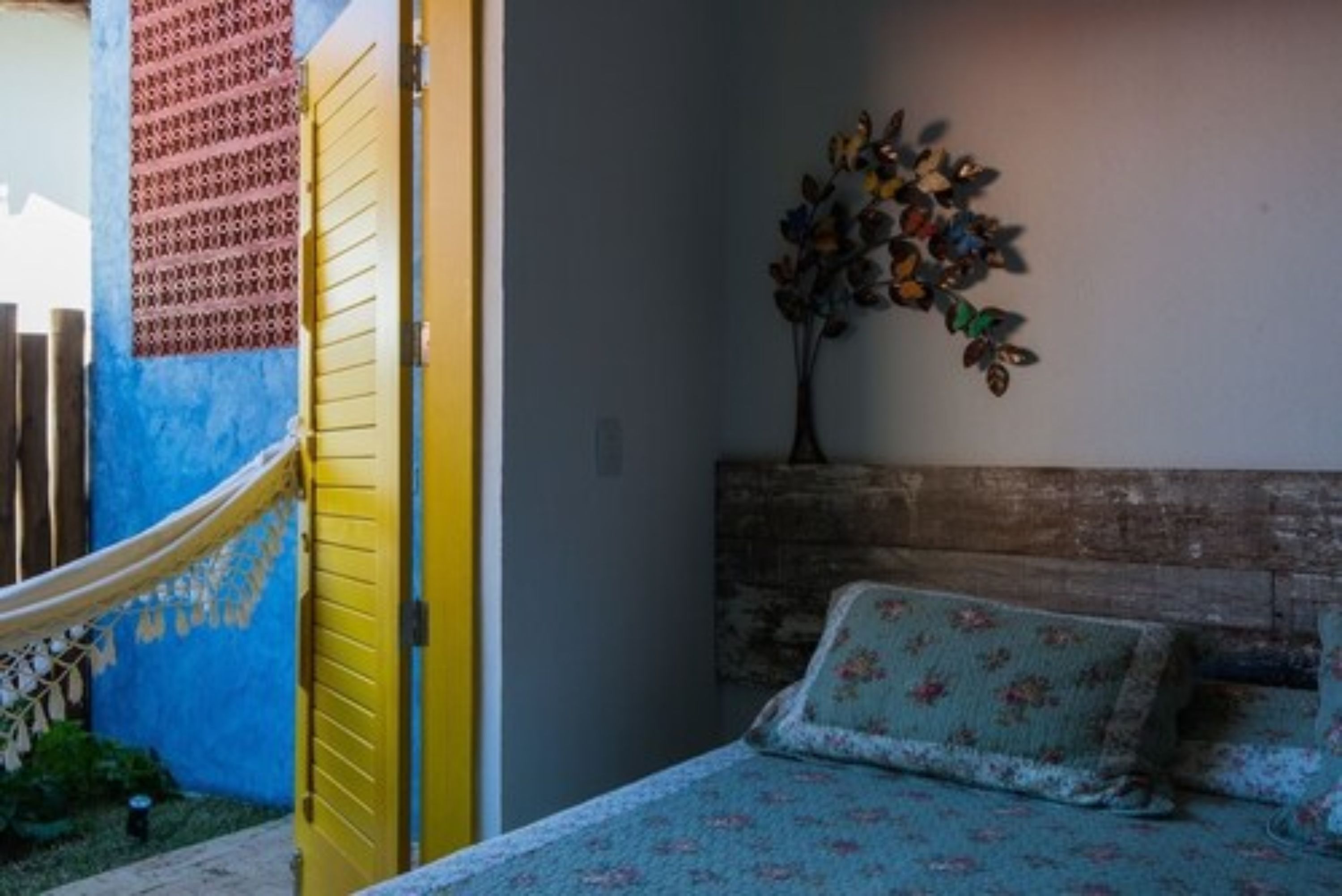 Quarto com cama, rede, planta suspensa na parede e parede estampada.