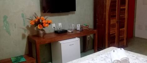 A room with a bed, a wooden desk with a television, a small refrigerator, and a wooden wardrobe.