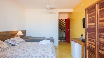 Un dormitorio con cama, escritorio, silla, lámpara, ventilador de techo y una puerta roja que da a una escalera.