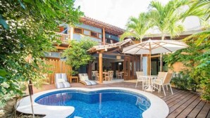 Une piscine avec une terrasse en bois, des chaises longues et un espace patio couvert.