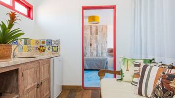 A compact room with a kitchenette, a bed with patterned pillows, and a view through a door.