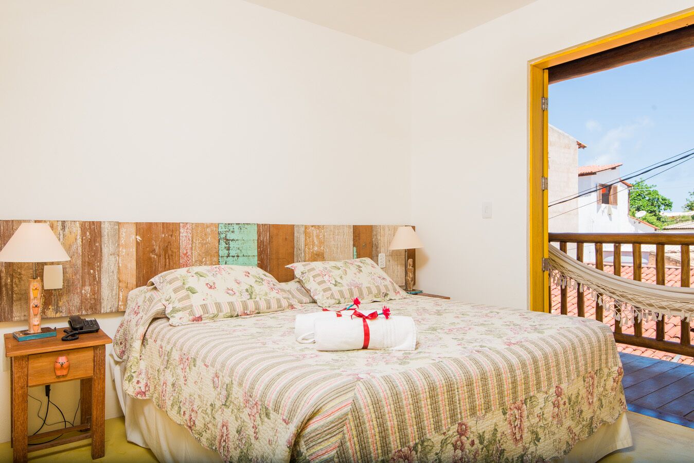 Quarto com cama, duas mesas de cabeceira, um criado-mudo e uma rede, com vista para o exterior.