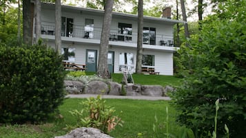 A two-story building with a balcony on the upper floor, surrounded by greenery and trees.