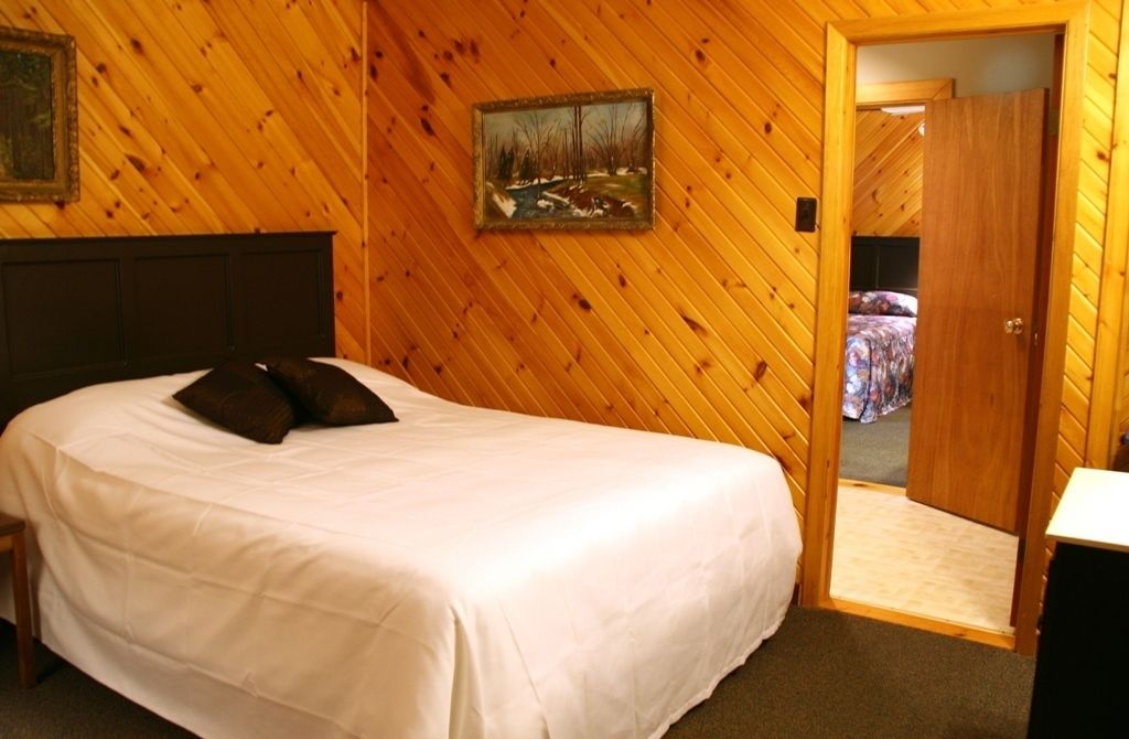 Una camera da letto con parete rivestita in legno, un letto con biancheria bianca e una porta che conduce in un'altra stanza.