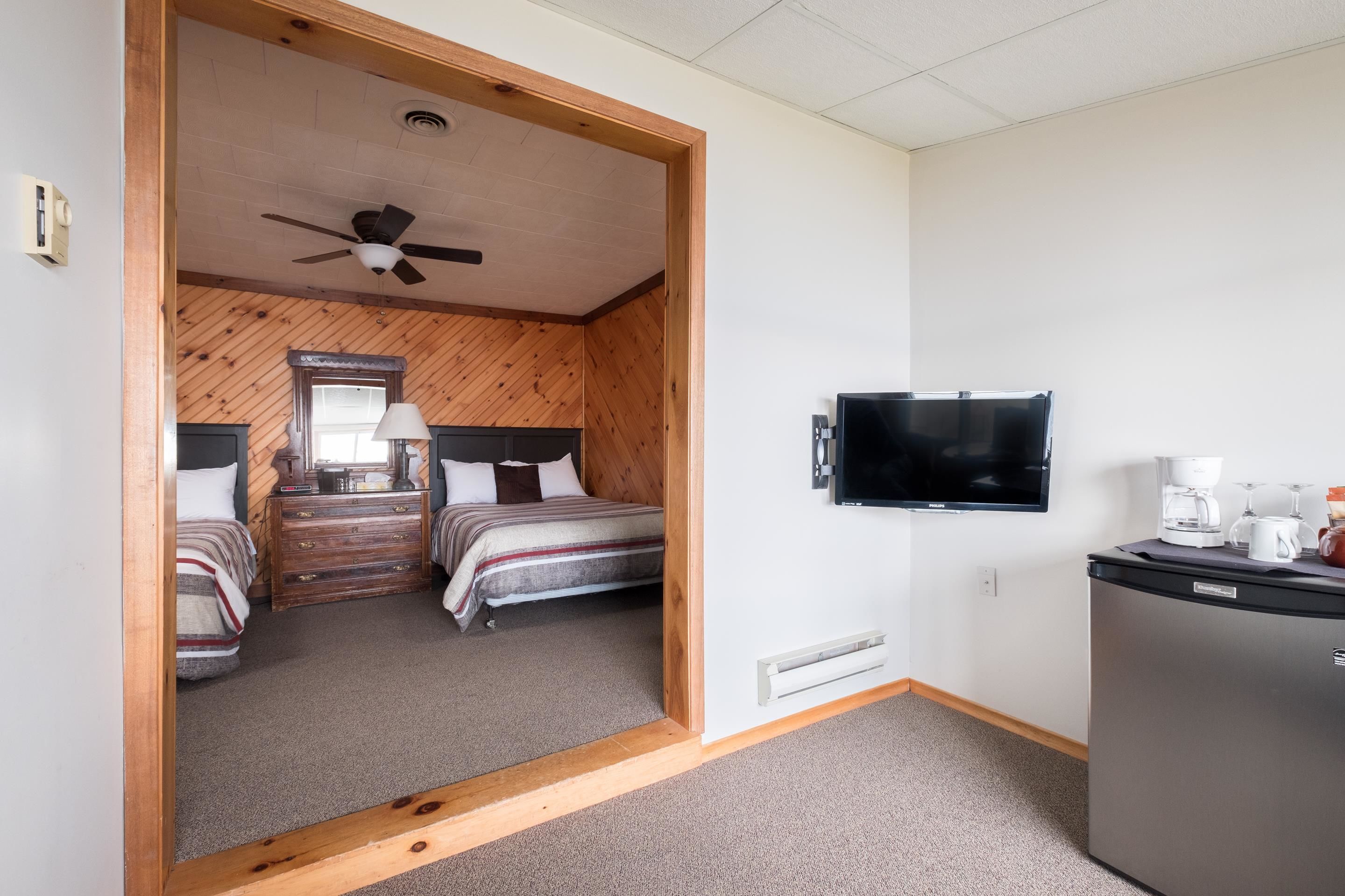 Ein Zimmer mit zwei Betten, einem Deckenventilator, einem Fernseher und einem Kühlschrank.