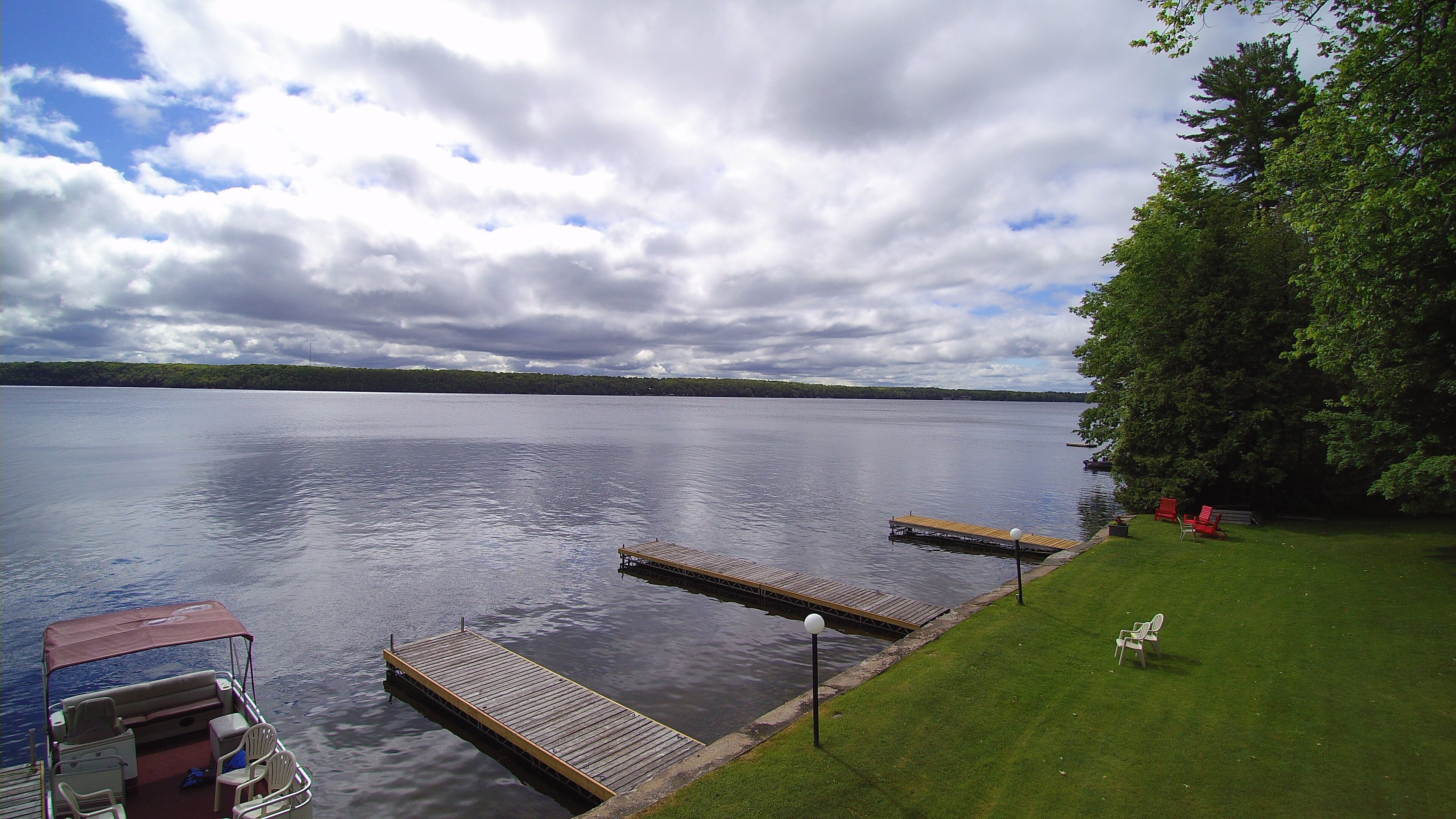 A calm lake with wooden docks extending into the water, surrounded by a grassy area with a bench and chairs.