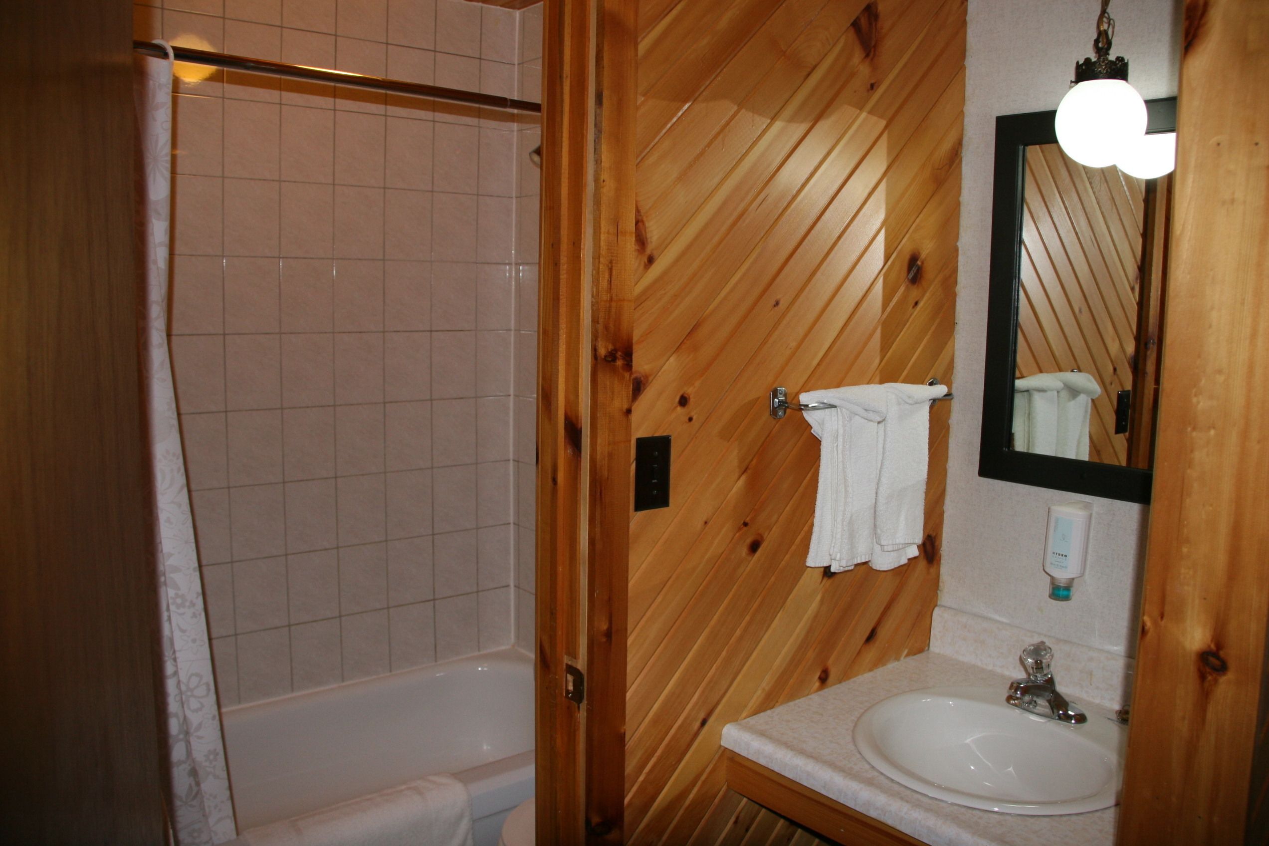 Une salle de bain aux murs lambrissés, équipée d’une baignoire, d’un lavabo et d’un miroir.
