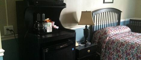 A hotel room with a bed, a desk with a microwave, a lamp, and a small cabinet.