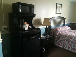 A hotel room with a bed, a desk with a microwave, a lamp, and a small cabinet. - Mamaroneck Motel (Mamaroneck)