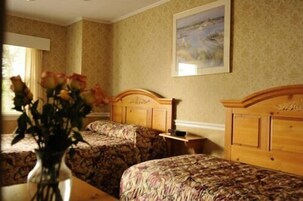 A hotel room with two beds, a wooden headboard, a vase with flowers, and a painting on the wall.