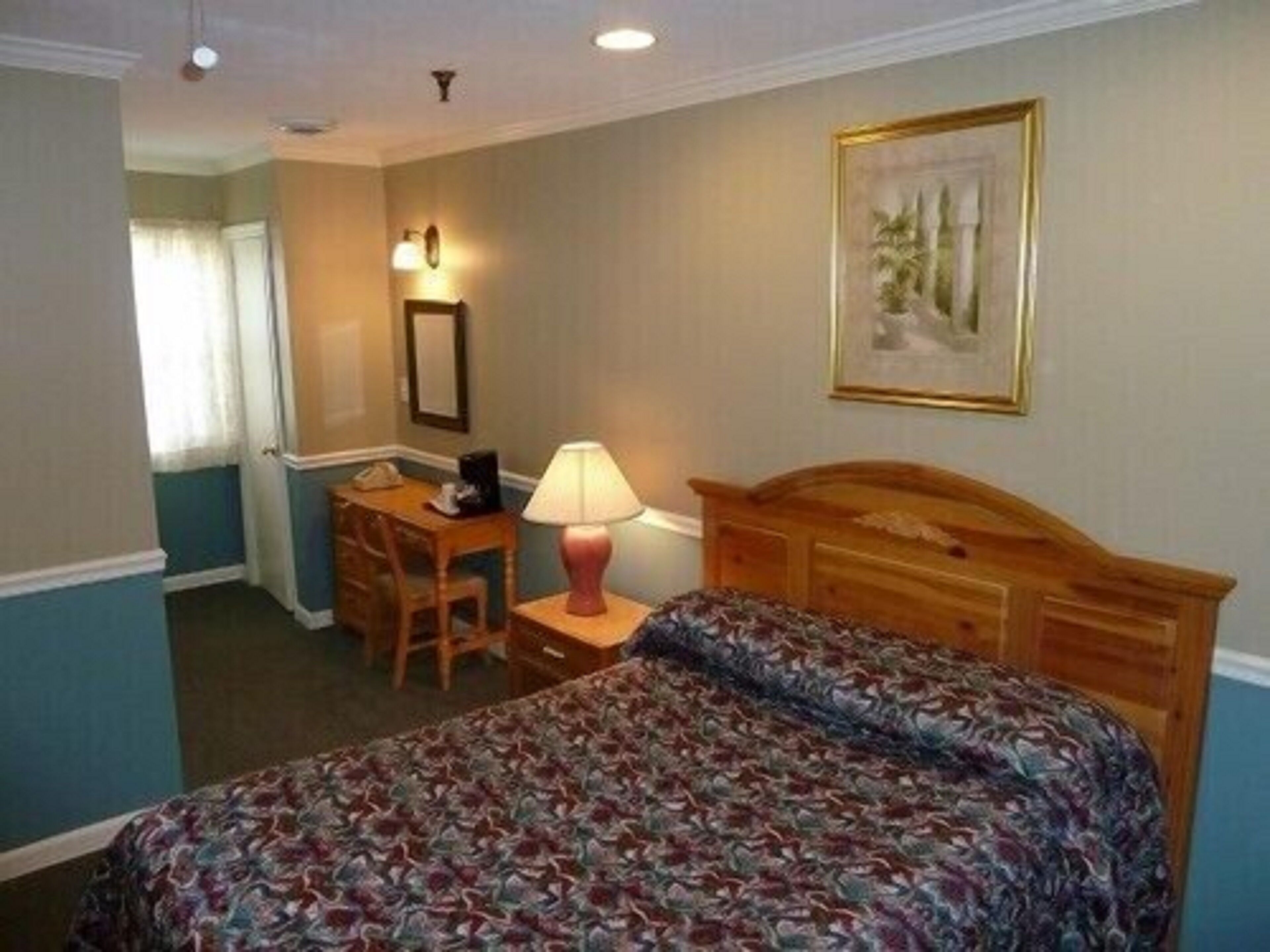 Ett hotellrum med en säng, ett skrivbord, en stol, en lampa och en inramad tavla på väggen.