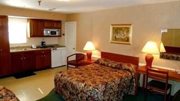 A hotel room with a bed, a desk, a chair, a microwave, and a small kitchenette.