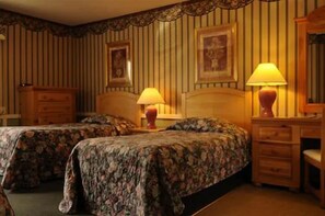 A hotel room with two beds, each with floral bedspreads, a wooden dresser, and two wall-mounted lamps. - Mamaroneck Motel (Mamaroneck)
