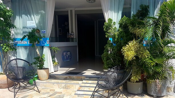 Entrada de hotel con un patio empedrado, dos sillas negras, plantas en macetas y un cartel que indica un restaurante cercano.
