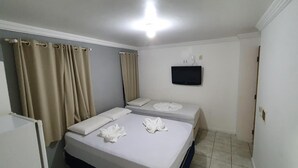 Habitación de hotel con dos camas, cortinas color beige, un televisor de pantalla plana y un ventanal pequeño.