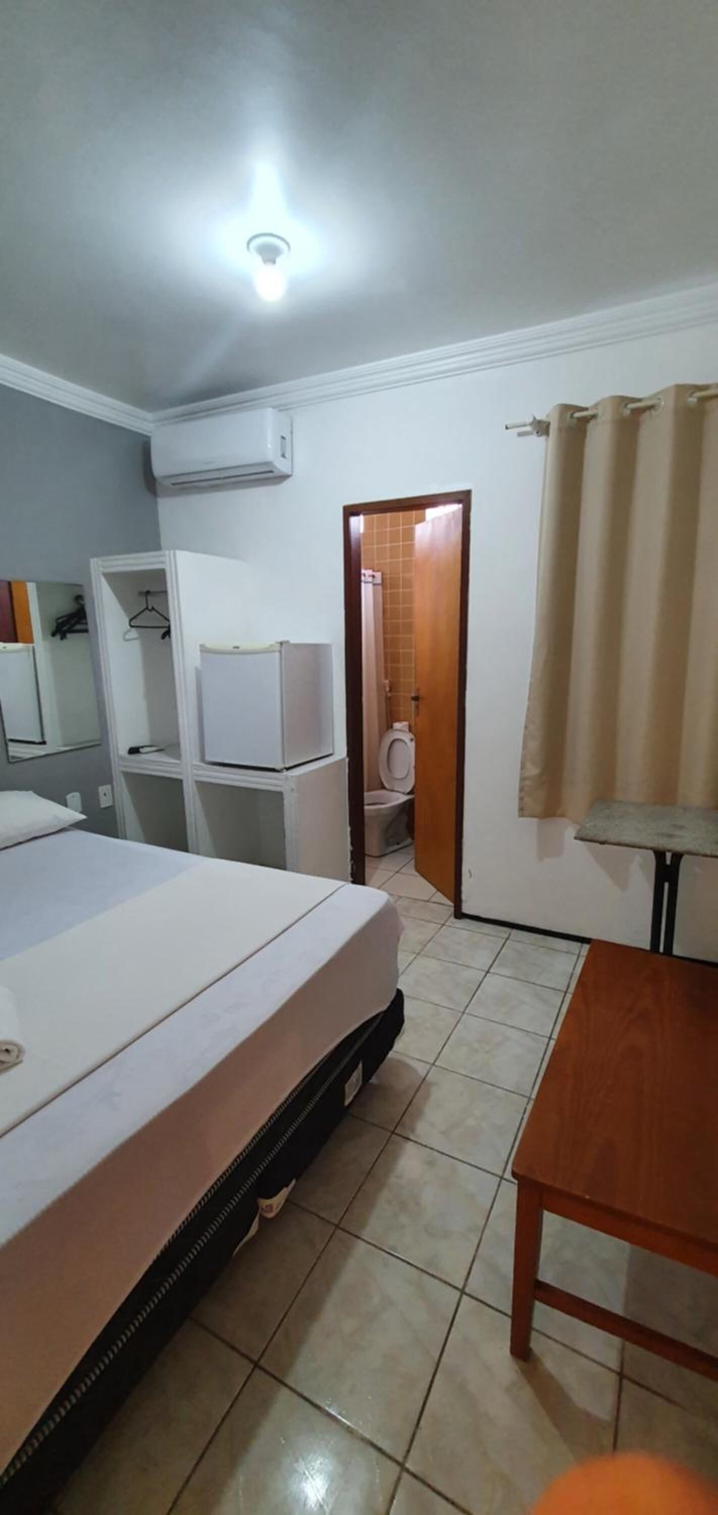 Habitación de hotel con cama, escritorio, equipo de aire acondicionado, baño con inodoro y puerta que da a otra habitación.