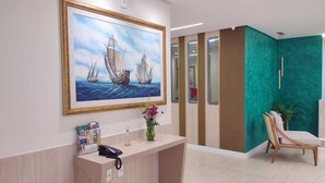A reception area with a painting of sailboats, a reception desk, a phone, and a chair. - Hotel Três Caravelas (Fortaleza)